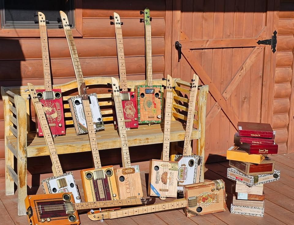 A lineup of 3-string cigar box guitars and amps on a bench